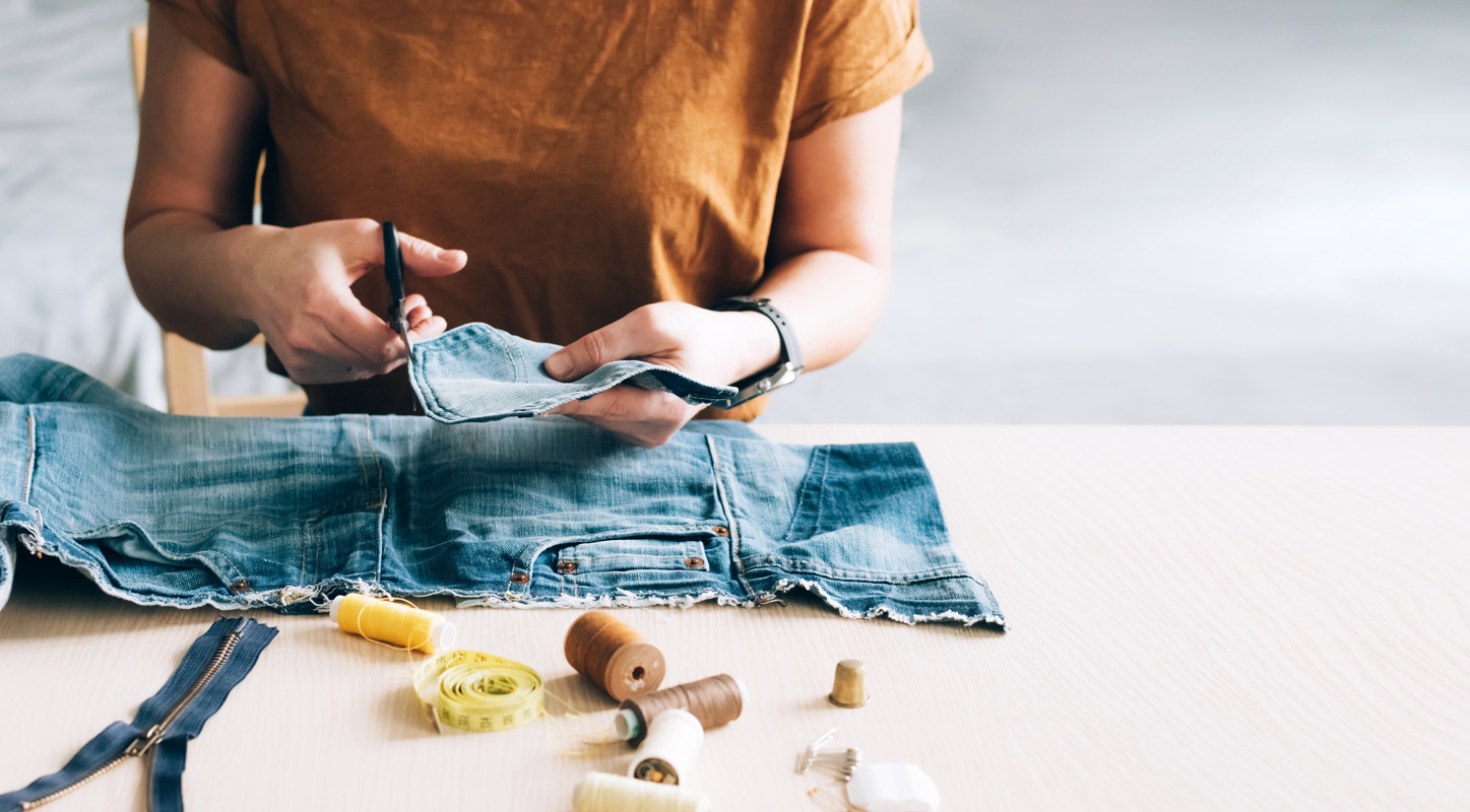 Woman repairs sews reuses fabric from old denim clothes economical reuse